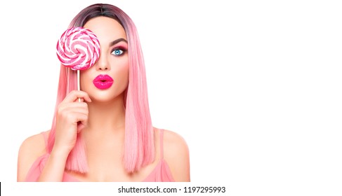 Surprised sexy girl eating lollipop. Beauty Glamour Model woman with trendy pink hair style and beautiful makeup holding pink sweet colorful lollipop candy, isolated on white background. Sweets