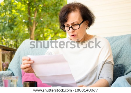 Surprised shocked senior woman n eyeglasses reading paper document or postal letter feeling frustrated by unexpected news sitting on sofa on home terrace. Received bank account balance or bad notice Foto stock © 