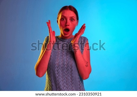 Surprised, shocked. Studio shot of amazed young girl looking at camera with astonished face over blue background in neon light. Concept of human emotions, mood, ad, mental health