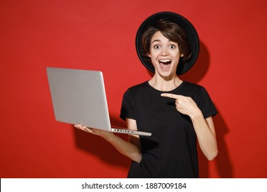 Surprised Shocked Young Brunette Woman 20s Years Old Wearing Casual Basic Black T-shirt Hat Pointing Index Finger On Laptop Pc Computer Say Wow Isolated On Bright Red Color Background Studio Portrait