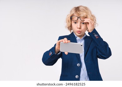 Surprised small preteen boy male child kid elementary primary middle school pupil teenager using cellphone mobile in formal clothes uniform eyeglasses isolated on white background. Education concept - Powered by Shutterstock