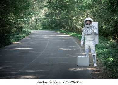 Surprised spaceman wearing full armor is standing near road in forest and looking at camera with smile. Full length portrait. Copy space on left side