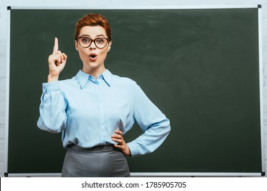 surprised teacher showing idea gesture while standing with hand on hip near chalkboard - Powered by Shutterstock