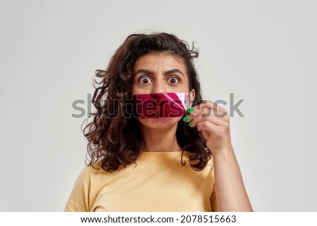 Surprised woman with curly hair holding purple film in front of her mouth, looking amazed at camera, posing isolated over light background. Freestyle, human emotions, fun concept