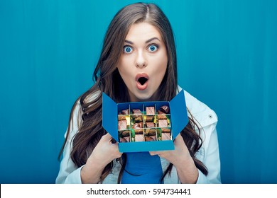 Surprised Woman Holding Blue Box With Chocolate  Candy. Blue Wall Background.