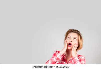 Surprised woman looking up with open mouth, holding hands her face 