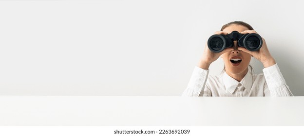 Surprised woman looking through binoculars peeking out from behind white cardboard. Banner. - Powered by Shutterstock