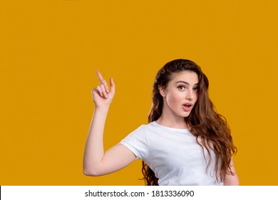 Surprised Woman Portrait. Aha Moment. Shocked Lady With Open Mouth Pointing Up At Copy Space Isolated On Orange Wall. Eureka Effect. Found Solution. Insight Idea. Advertising Background.