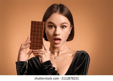 Surprised woman with sweet chocolate on color background