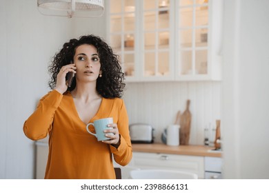 Surprised woman talking phone at home with puzzled face expression received breathtaking news, crisis, failure. Housewife at kitchen,