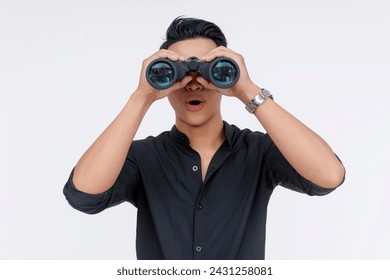 Surprised young Asian man using a pair of binoculars, showing an expression of shock and amazement, isolated on white.