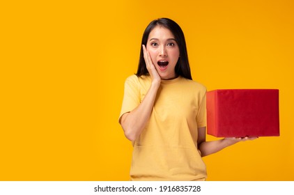 Surprised young asian woman holding red gift box and get shock by open mouth Standing over yellow background Beautiful Asia girl happy smile hold new year gift box present Using for advertisement