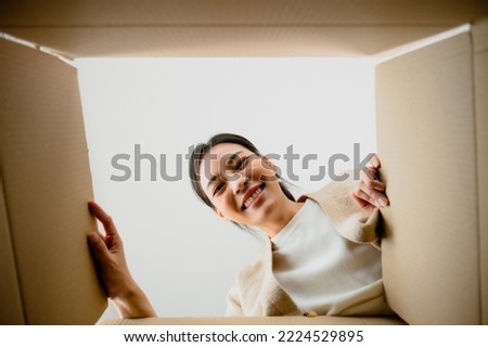 Surprised young asian woman unpacking. Opening carton box and looking inside. Packaging box, delivery service. Human emotions and facial expression