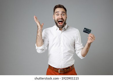 Surprised Young Bearded Business Man In Classic White Shirt Stand Hold Credit Bank Card Screaming Spreading Hands Isolated On Grey Color Background Studio Portrait. Achievement Career Wealth Concept