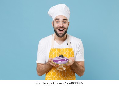 Surprised Young Bearded Male Chef Or Cook Baker Man In Apron White T-shirt Toque Chefs Hat Isolated On Blue Background Studio Portrait. Cooking Food Concept. Mock Up Copy Space. Hold Dessert Cake