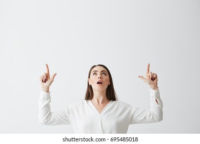 Surprised young beautiful brunette businesswoman smiling looking pointing fingers up over white background.