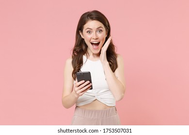 Surprised young brunette woman girl in light casual clothes isolated on pastel pink background. People lifestyle concept. Mock up copy space. Using mobile phone, typing sms message, put hand on cheek - Shutterstock ID 1753507031