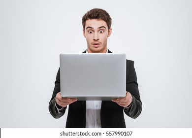 Surprised Young Business Man In Black Suit Standing And Holding Laptop Isolated On A White Background