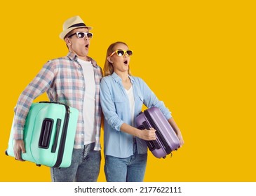 Surprised young Caucasian man and woman tourists in sunglasses holding suitcases for travel dumbfounded by lucrative invitation to tour or cheap offer from airline company stand on yellow background