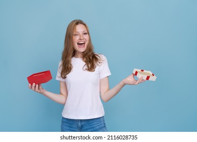 Surprised Young Caucasian Woman Holding Red Gift Box And Shocked With Open Mouth Standing On Blue Background Beautiful Girl Happy Smile Holding Generic Box Suitable For Any Holiday Use For Advertising