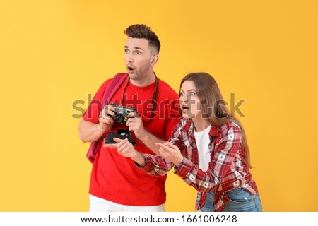 Surprised young couple with camera pointing and looking away, travel and discovery concept, isolated on yellow background