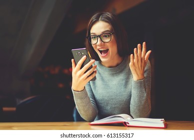 Surprised young female blogger chatting with best friends in social network on mobile phone while received shocking good news using wifi zone and reading interesting book indoors after work - Powered by Shutterstock