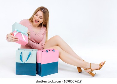 Surprised young girl in summer clothes sits on the floor with a shopping bag looking what she bought, isolated on white background studio portrait. Shopping discount sale concept.
