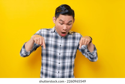 Surprised young handsome Asian man wearing a plaid shirt pointing fingers down, inviting customers to special event isolated on yellow background. People lifestyle concept - Powered by Shutterstock