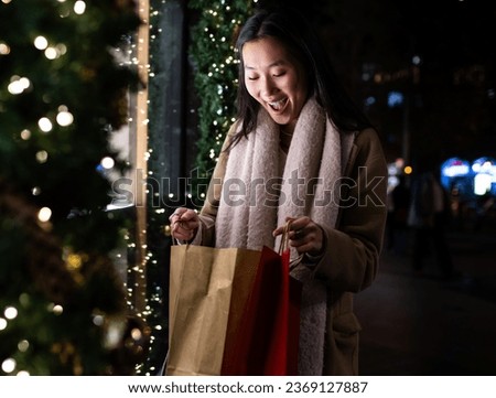 Surprised young lady looking inside shopping bags in the street. Cheerful female holding shopping bags in Christmas at night.