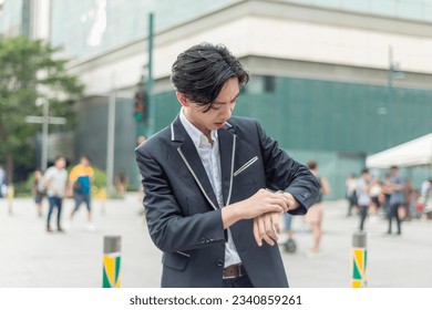 A surprised young male employee realizes that he late upon checking his watch. Outdoor city plaza scene. - Powered by Shutterstock