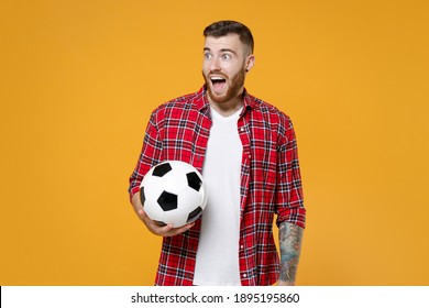 Surprised Young Man Football Fan In Basic Red Shirt Cheer Up Support Favorite Team With Soccer Ball Looking Aside Isolated On Yellow Background Studio Portrait. People Sport Leisure Lifestyle Concept