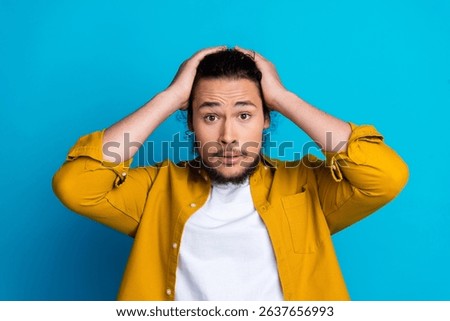 Surprised young man gesturing with hands on head against a bright blue background showcasing emotion and self-expression