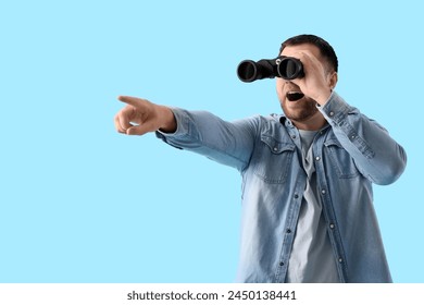 Surprised young man looking through binoculars and pointing at something on blue background - Powered by Shutterstock