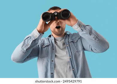 Surprised young man looking through binoculars on blue background - Powered by Shutterstock