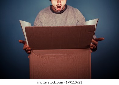 Surprised Young Man Is Opening A Large Cardboard Box With Something Exciting Inside It