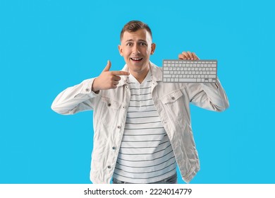 Surprised young man pointing at computer keyboard on blue background