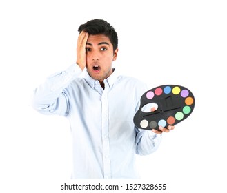 Surprised Young Man Putting His Hand On His Face While Holding A Colour Palette Against A White Background