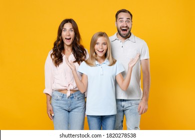 Surprised Young Parents Mom Dad With Child Kid Daughter Teen Girl In Basic T-shirts Keeping Mouth Open Spreading Hands Isolated On Yellow Background Studio Portrait. Family Day Parenthood Concept