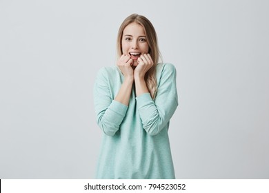 Surprised young pretty female with long blonde hair, looks with opened mouth at camera, excited to see something pleasant, dressed casually. Surprisment and facial expression