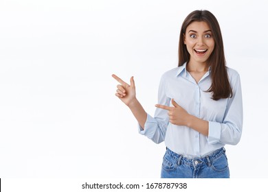 Surprised young successful working woman in blue blouse look impressed as seeing something unexpecting and awesome, pointing finger left sharing great news with you, white background