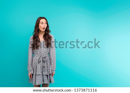 Surprised young woman in a dress isolated over turquoise blue background