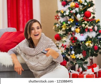 Surprised Young Woman Watching TV Near Christmas Tree