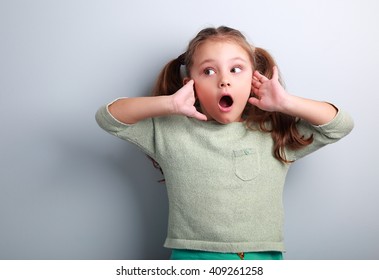 Surprising Kid Girl With Long Hair With Opened Mouth And Hand Near Face Looking On Blue Copy Space Background