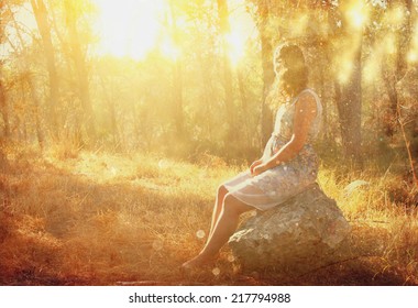 surreal blurred background of young woman sitting on the stone in forest. abstract and dreamy concept. image is textured and retro toned