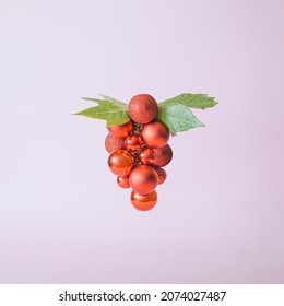 Surreal Christmas Design With Shiny Red Baubles And Green Leaves Against Pastel Pink Background.