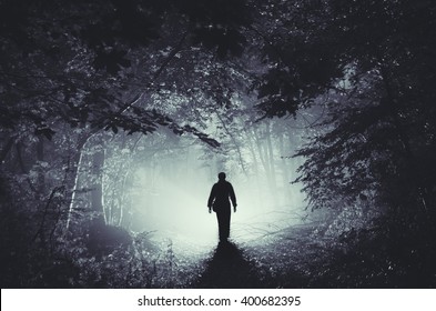 surreal light in dark forest and man silhouette