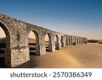 Surreal post apocalyptic fantastic scene with ancient aqueduct swallowed by the desert sand under the clear blue sky. Perspective abstract landscape, climate change, global warming concept