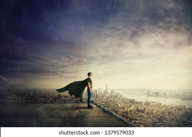 Surreal view of confident superhero with cape stands on the rooftop looking over city horizon. Ambition and business success concept. Leadership hero power, motivation and inner strength symbol. - Powered by Shutterstock