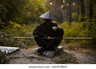 Surrealism theme: a man in a hannya mask, black kimono, black hat with a bamboo stick in his hands in the forest. Surreal image of a man in a hannya half mask, kimono. Surreal samurai, surreal ninja