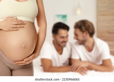 Surrogacy concept. Young pregnant woman and blurred view of happy gay couple indoors